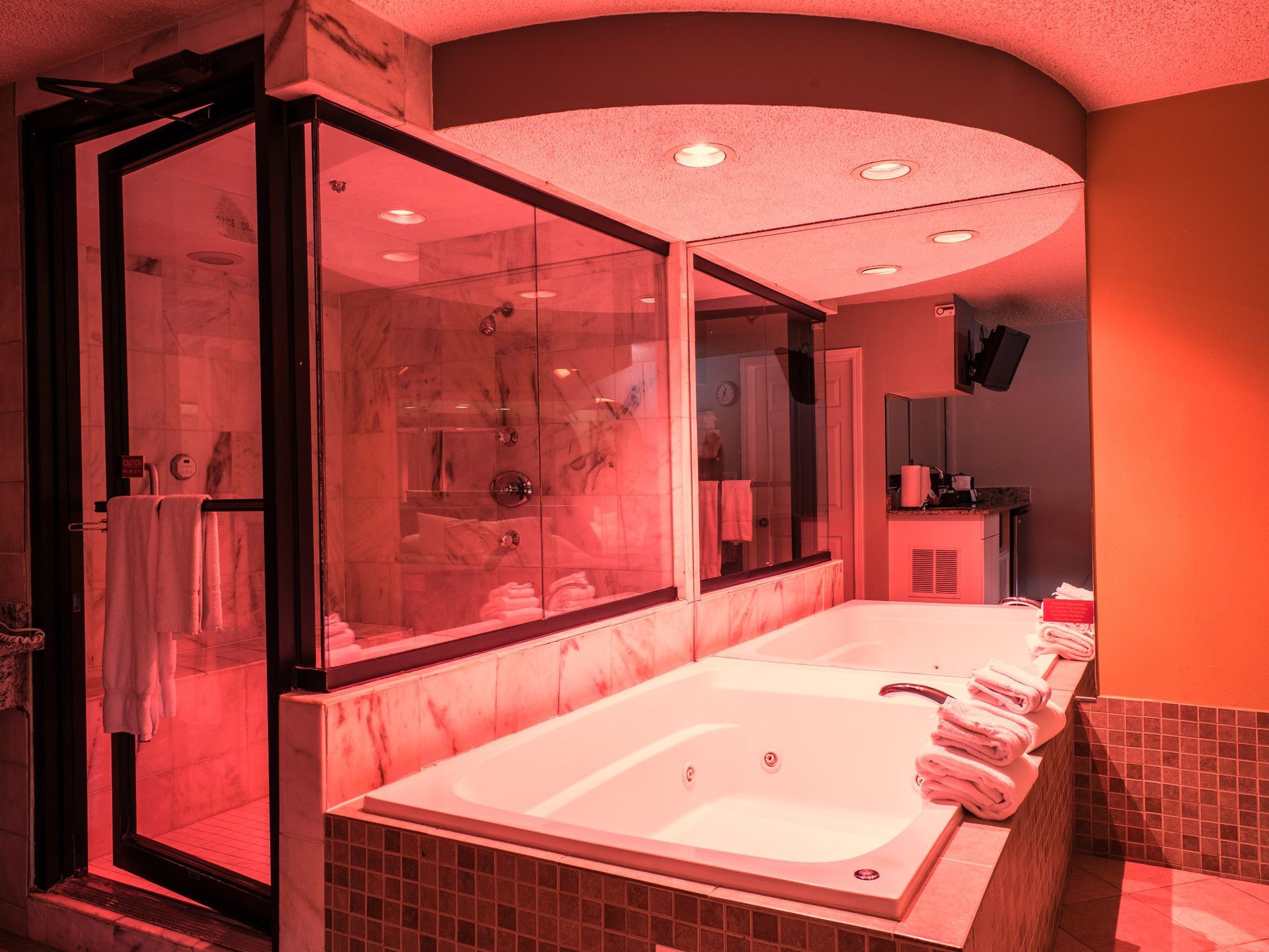 Bathroom with jacuzzi tub, glass shower, and towels, illuminated by red light.