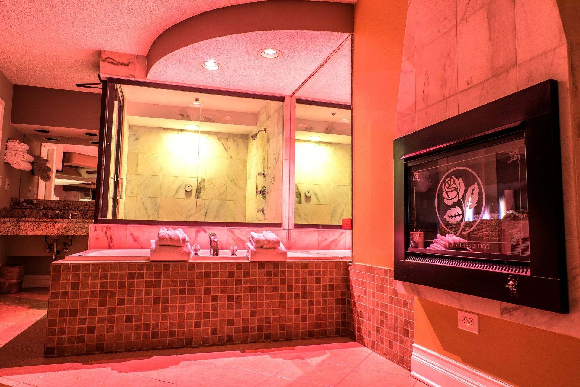 A bathroom with a jacuzzi, shower, and fireplace, lit in red, creating a romantic atmosphere.