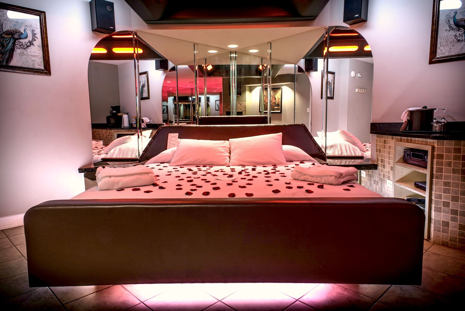 Romantic motel room with mirrored walls, heart petals on bed, and mood lighting.