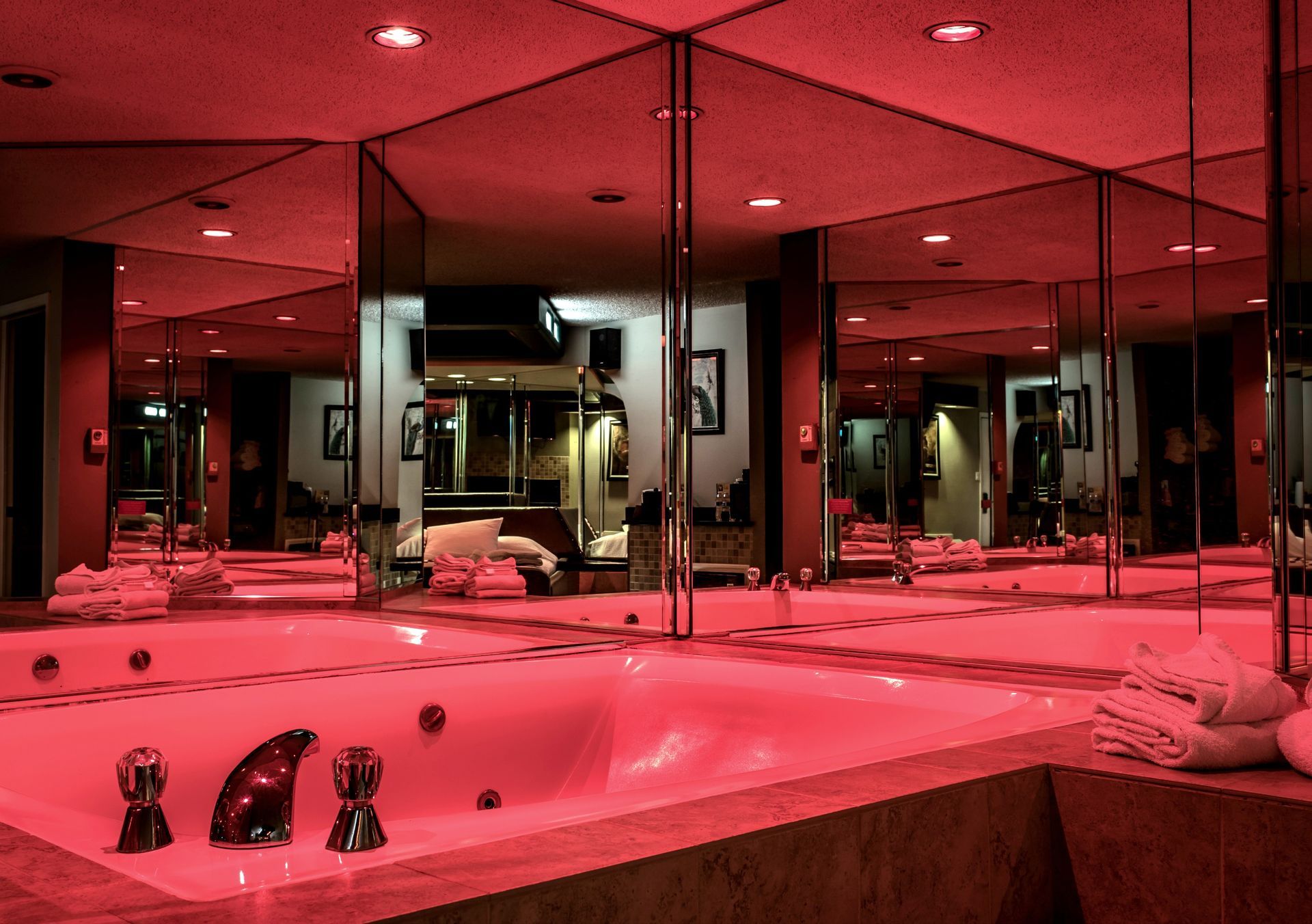 A jacuzzi in a mirrored room, illuminated by red light.