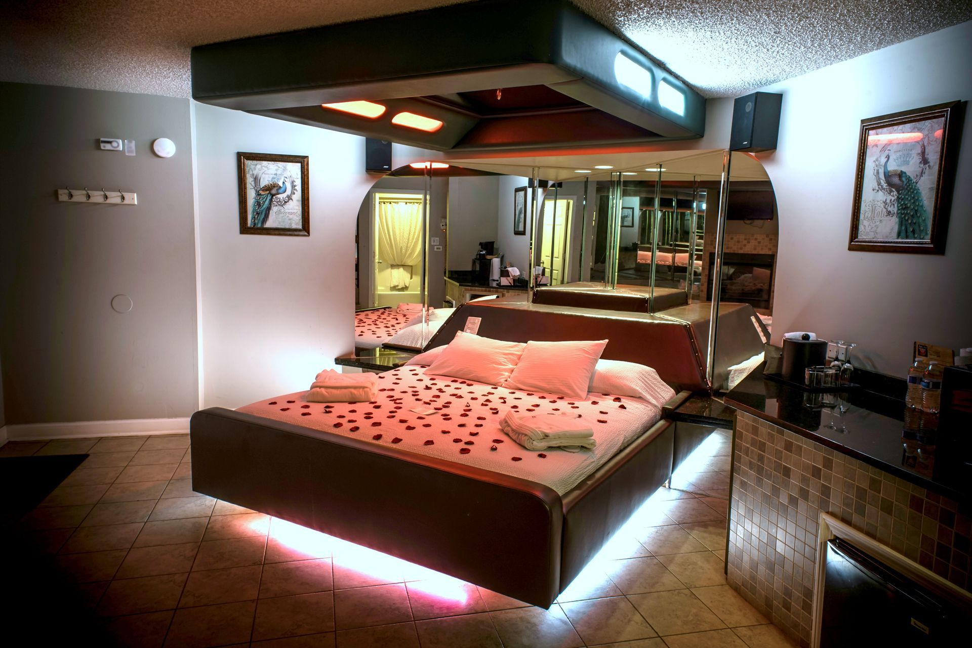Romantic hotel room with a bed, mirrors, and mood lighting. Red rose petals on the bed.