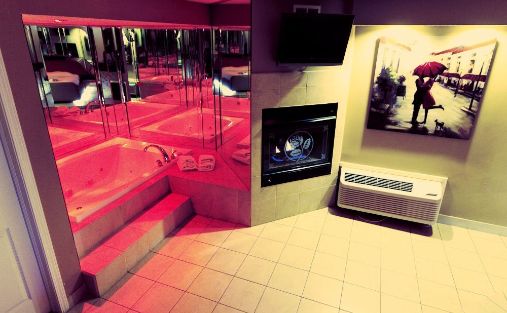 Hotel room with a jacuzzi, fireplace, and painting of a couple with umbrella.