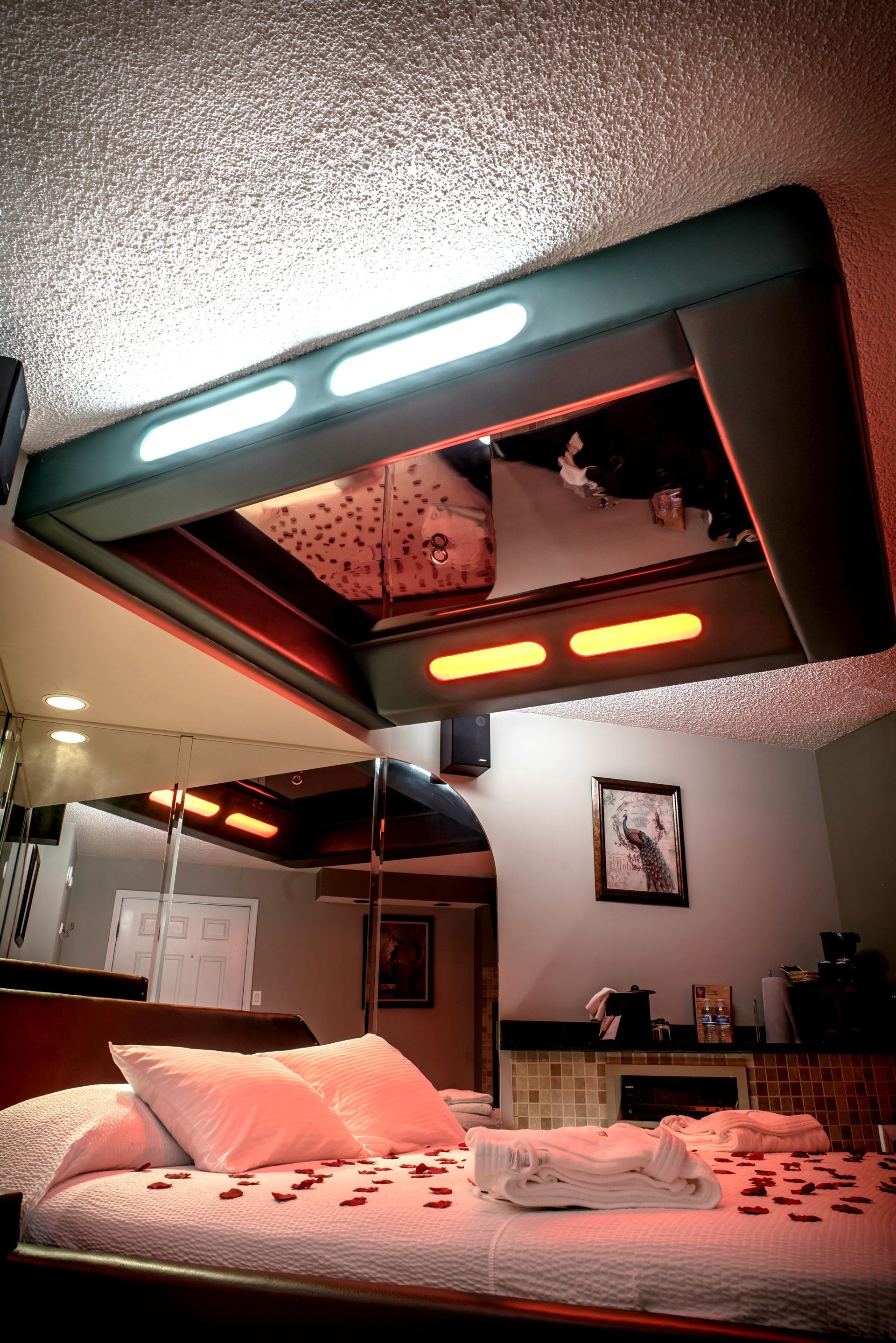 Romantic motel room with bed, mirrored ceiling, and red lighting.