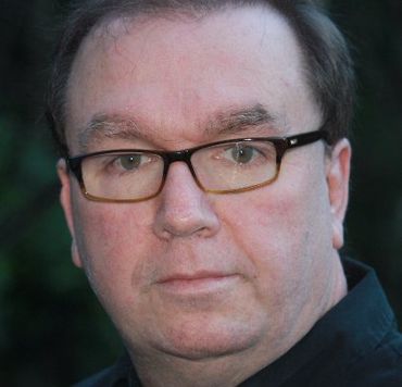Close-up portrait of a person wearing black glasses, looking at the camera with a neutral expression.