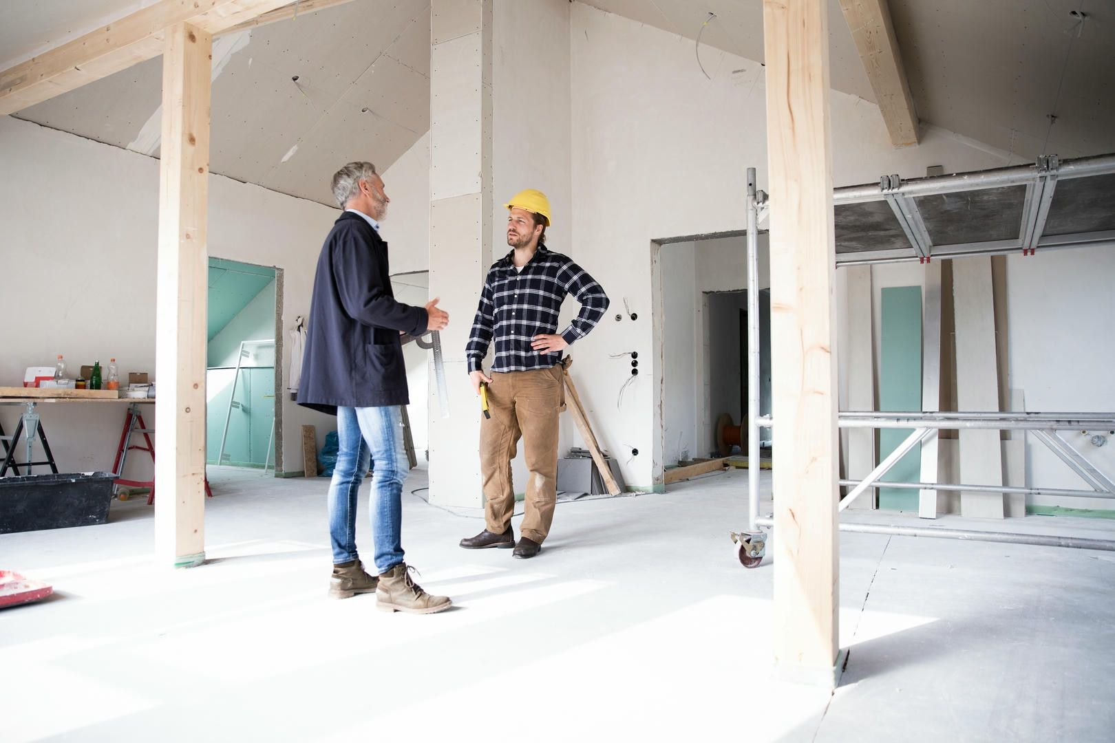 Two men in a construction site: one in a coat, the other in a hard hat, talking.