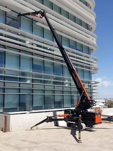Una piattaforma aerea arancione e nera si estende verso le finestre di un edificio moderno, all'aperto in una giornata di sole.