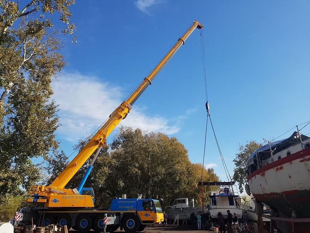 Una gru gialla solleva una barca in un cantiere navale in una giornata di sole.