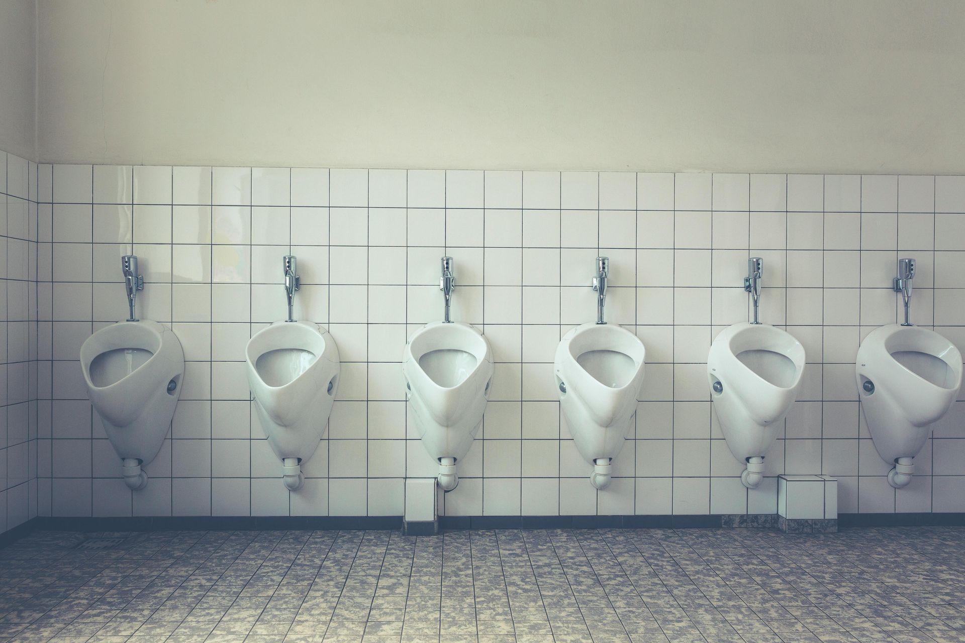 Row of white urinals on a tiled wall in a public restroom.