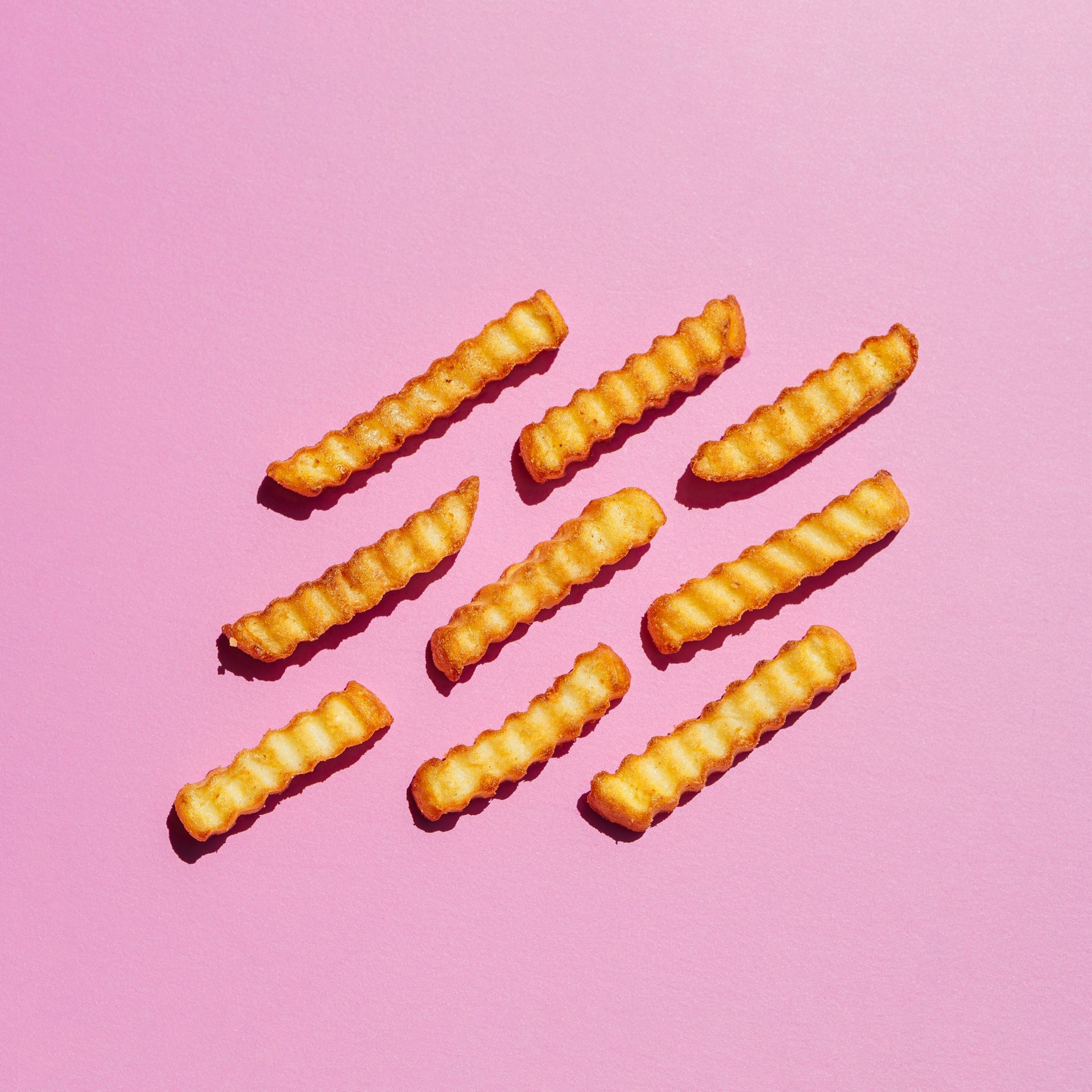 Frites ondulées disposées en diagonale sur un fond rose.