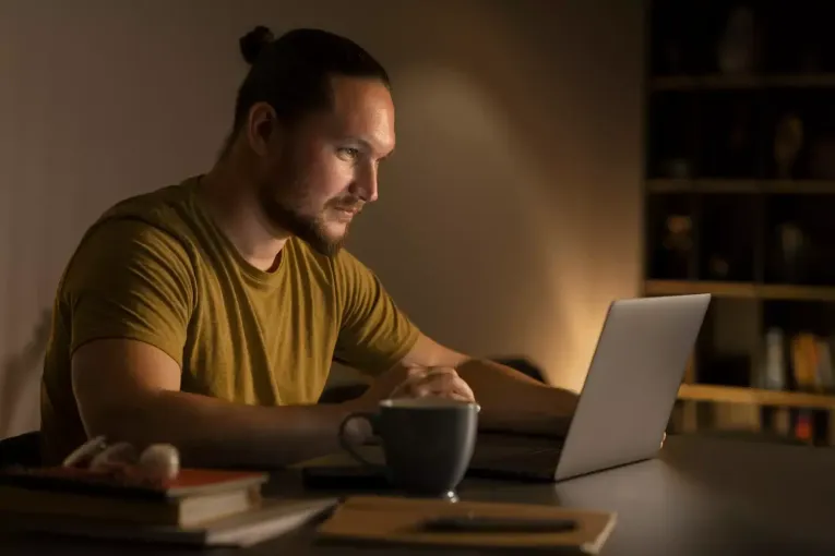 Um homem está sentado à mesa usando um laptop.