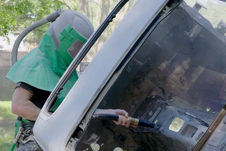 A man wearing a green helmet is sandblasting a car.