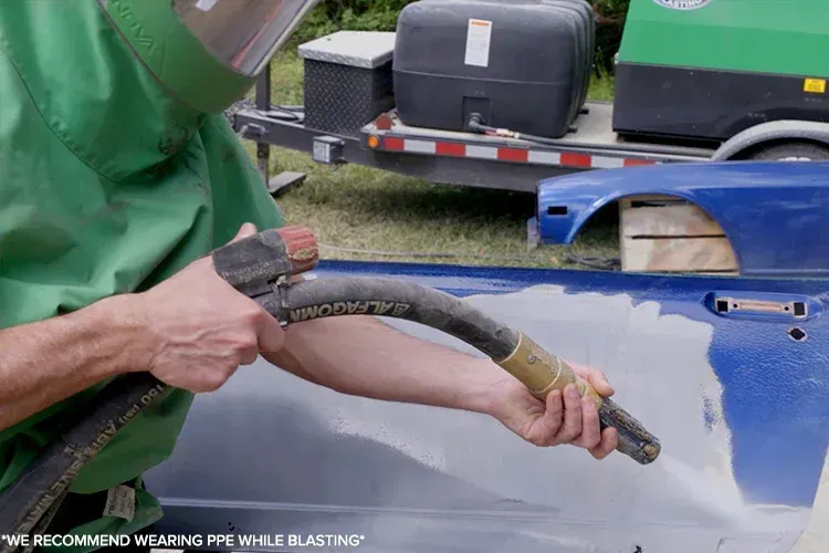 A man wearing a helmet is sandblasting a blue car door.