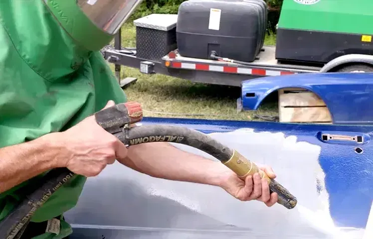 A man in a green shirt is sandblasting a blue car.