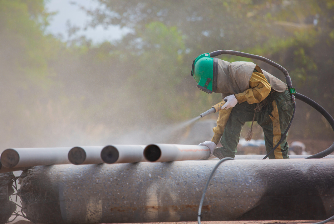 A man is sandblasting a pipe with a hose.