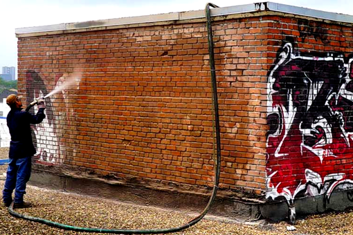 A man is spraying graffiti on a brick wall with a hose.