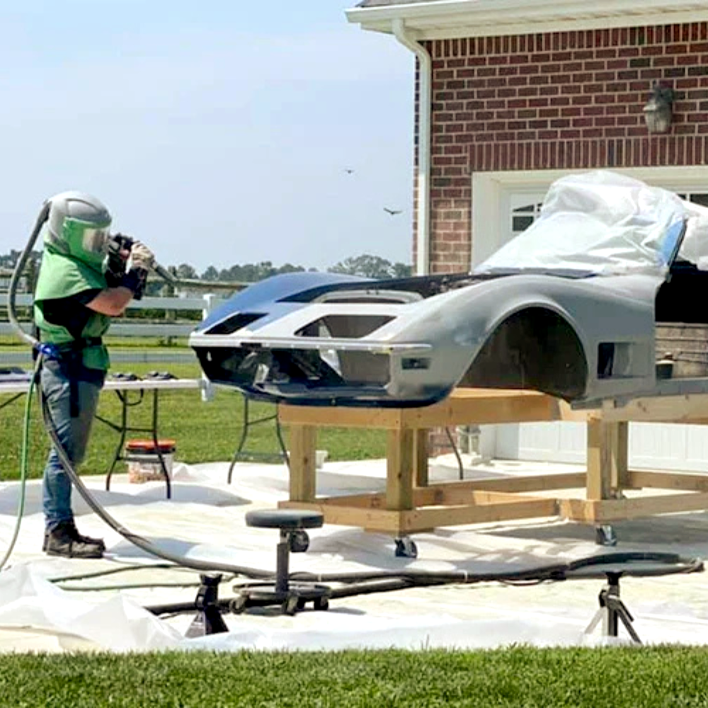 A man wearing a helmet is sandblasting a car
