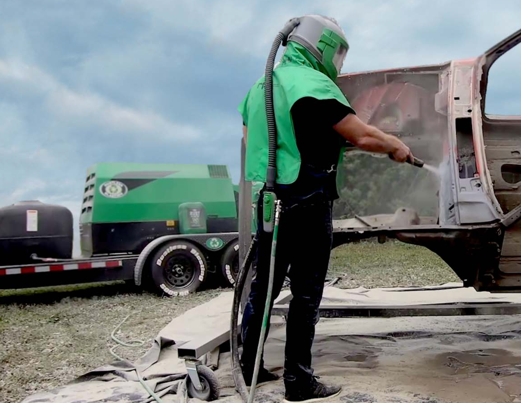A man in a green vest is sandblasting a truck