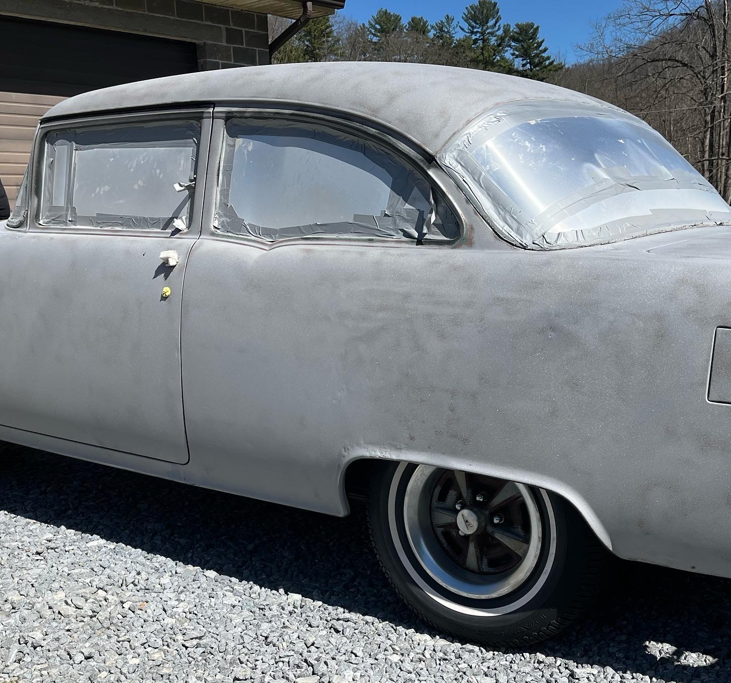 A black car is parked on gravel in front of a garage