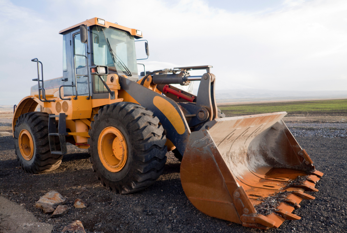 A bulldozer with a large orange bucket is parked on a dirt road.