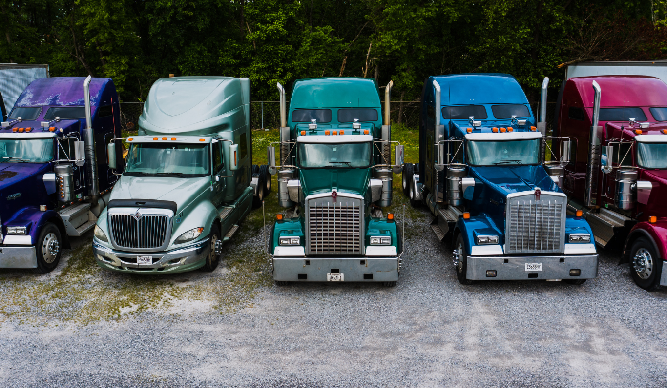 A row of semi trucks are parked in a gravel lot.