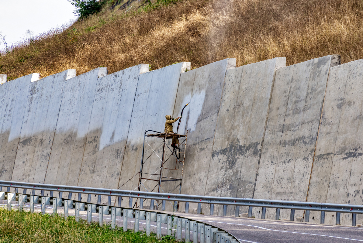 A man is painting a concrete wall next to a highway.