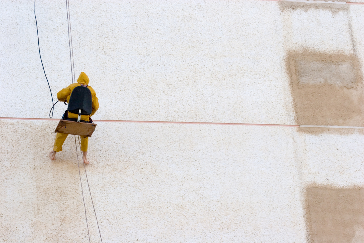 A man is painting a wall from a rope.