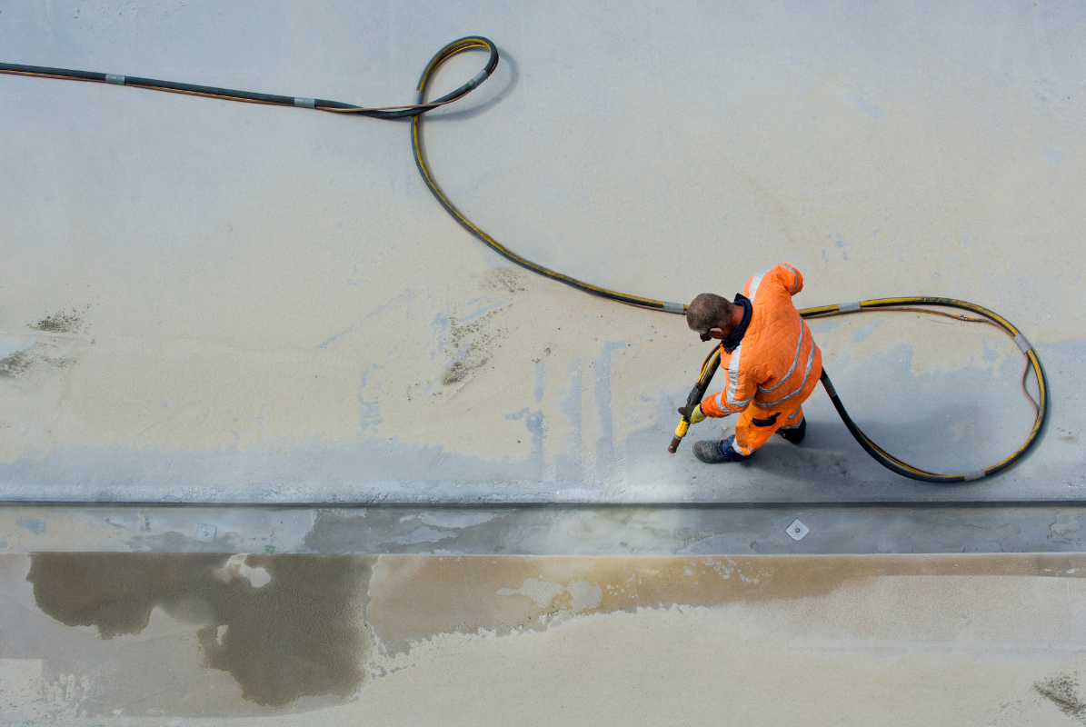 A man in an orange jumpsuit is cleaning a concrete surface with a hose.