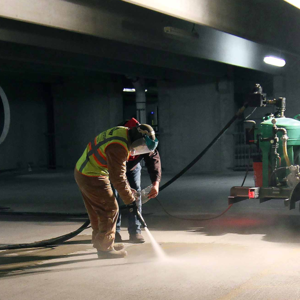 A man wearing a yellow vest sandblasting concrete to effectively clean it and restore it to new condition