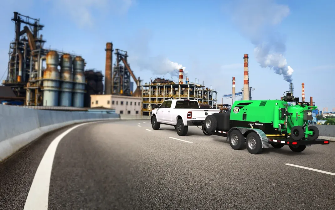 Two trucks are driving down a highway next to a factory.