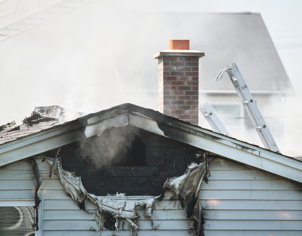 A house that has been damaged by a fire with smoke coming out of the chimney.