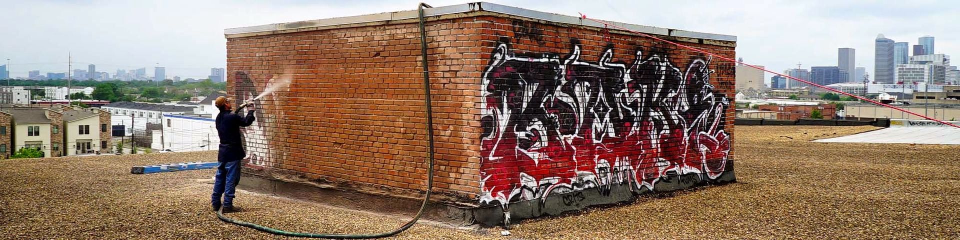 A man is standing in front of a brick building with graffiti on it.