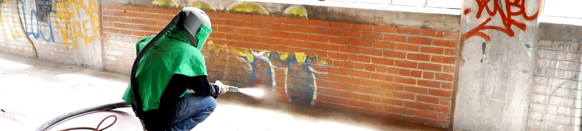 A person in a green hoodie is spray painting graffiti on a brick wall.