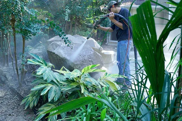 A man is cleaning a large rock with a dustless blasting hose and rig. 