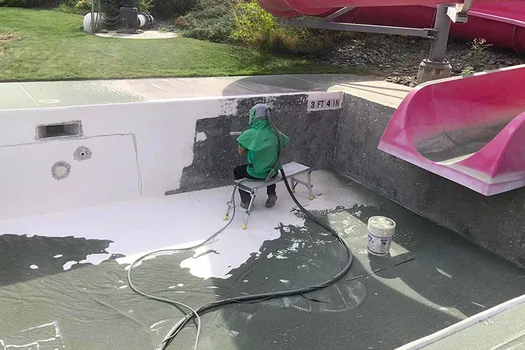 A person is painting a pool next to a water slide.