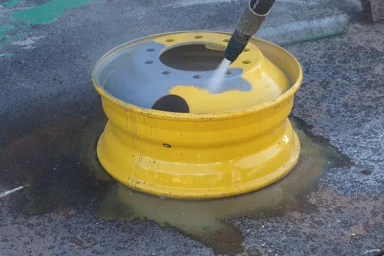 A yellow wheel is being cleaned with a high pressure washer.