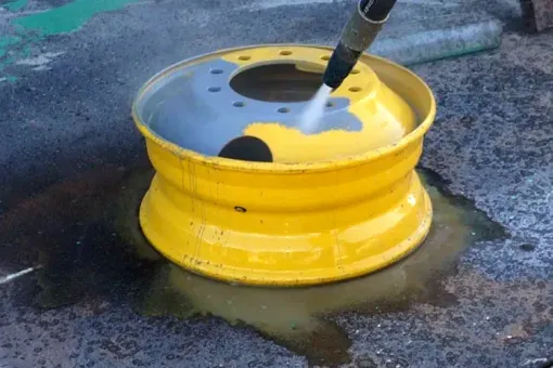 A yellow wheel is being cleaned with a high-pressure washer.