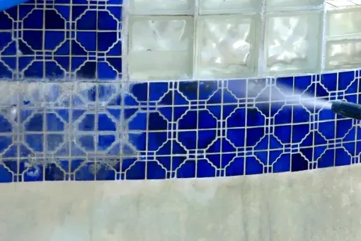 A person is cleaning a blue tile wall with a high pressure washer.