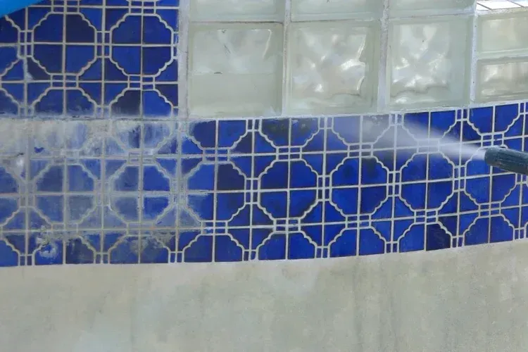A person is cleaning a blue tile wall with a high pressure washer.