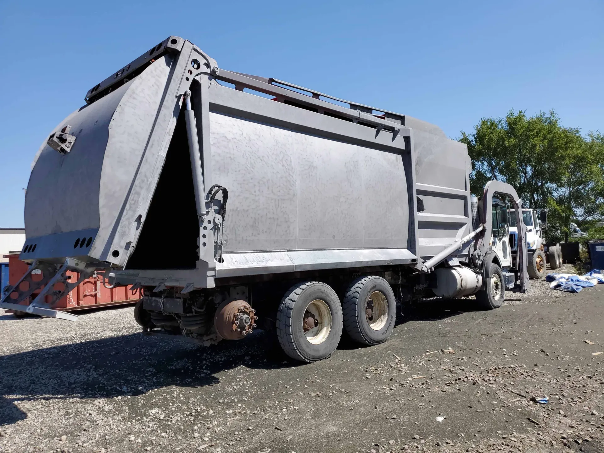 A garbage truck is parked in a gravel lot.