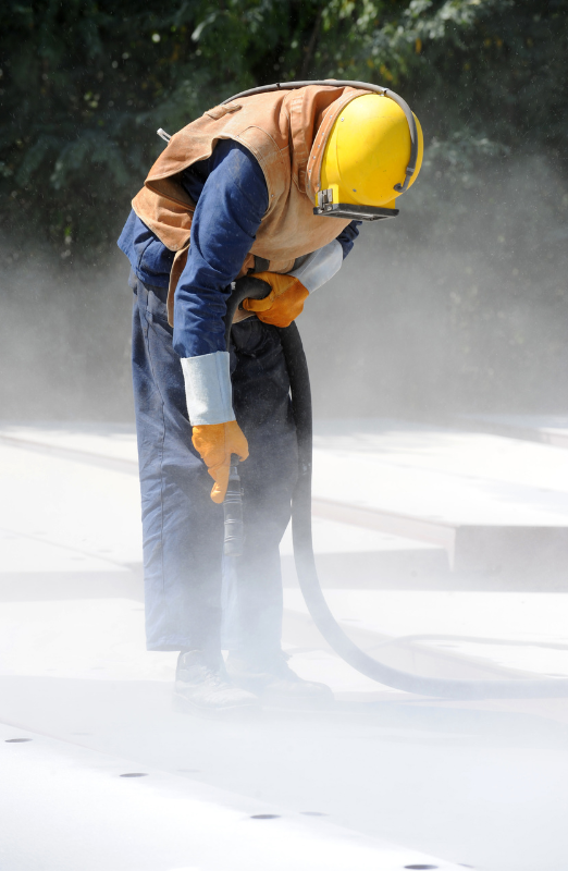 A man wearing a helmet and gloves is sandblasting a concrete surface.