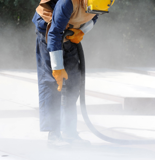 A man wearing a helmet and gloves is sandblasting a concrete surface.