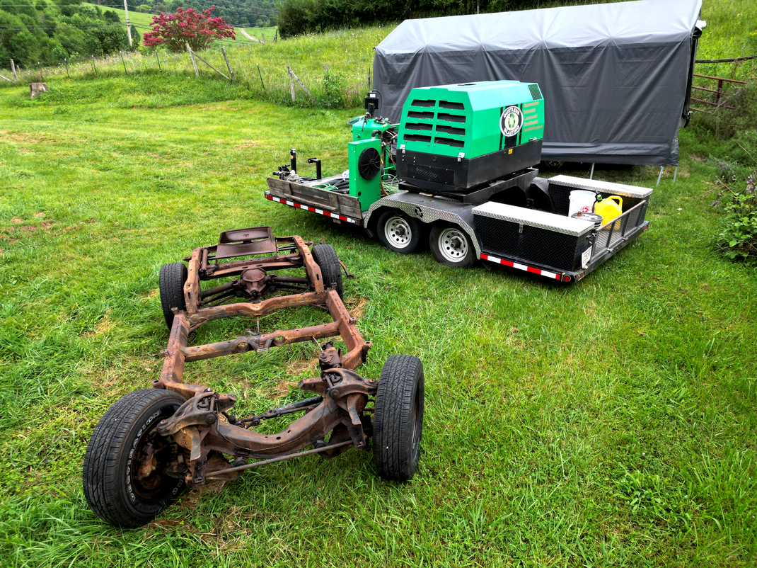A trailer with a green machine on it is parked in a grassy field.