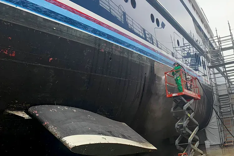 A man on a scissor lift is cleaning the side of a large ship.