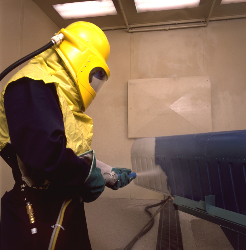 A man wearing a yellow helmet is spraying a blue object