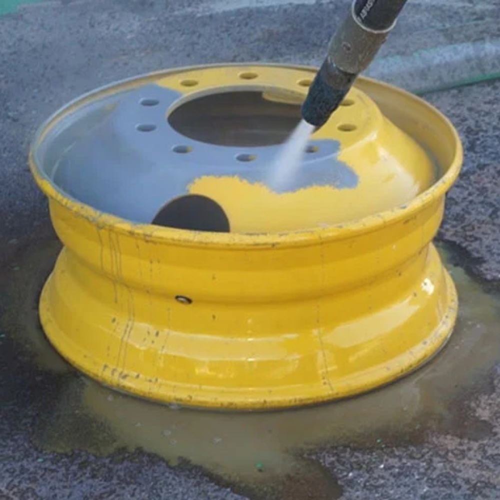 A yellow wheel is being cleaned with a high pressure washer.