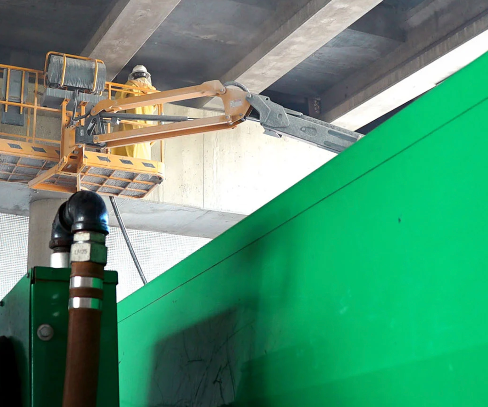 A yellow crane is hanging from the ceiling above a green wall.