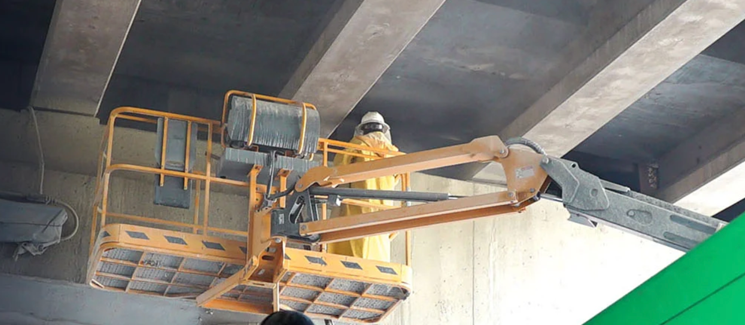 A man is standing on a lift under a bridge.