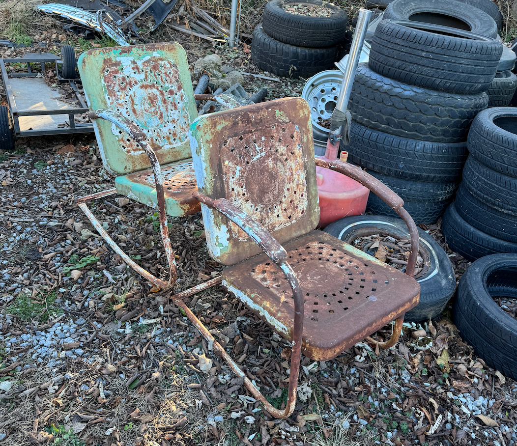 A rusty rocking chair is sitting in front of a pile of tires.