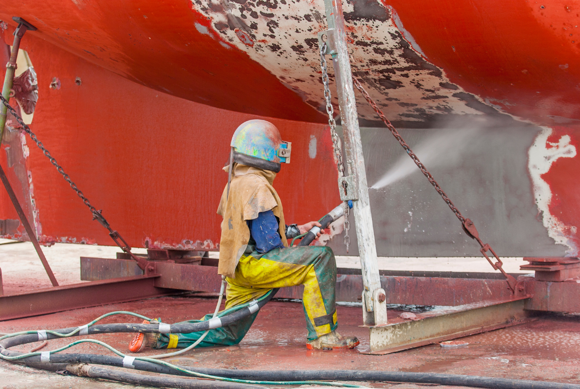 A man is sandblasting a boat with a machine.
