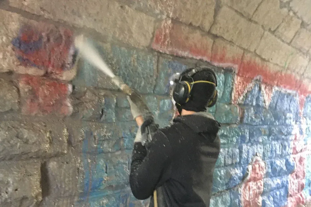 A man is cleaning graffiti on a brick wall with a high pressure washer.